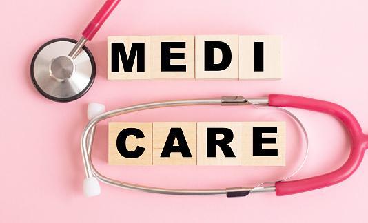 “Medicare” written on a wooden block and stethoscope on a pink background.