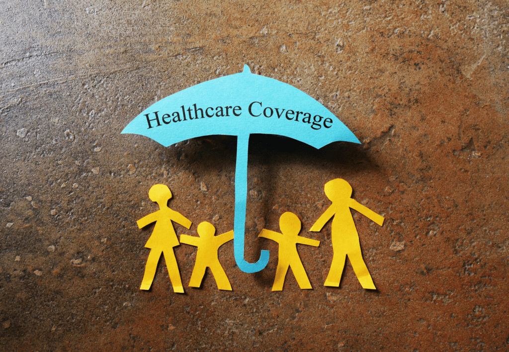 A paper cutout of an umbrella with the words “Healthcare Coverage” is held over a family of four.