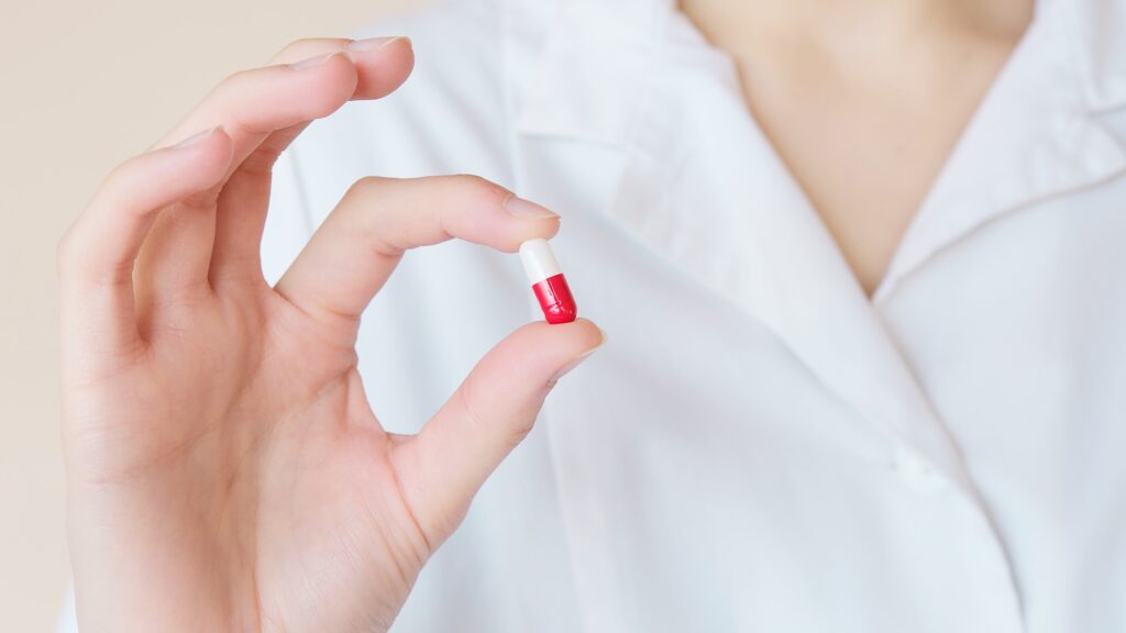 Closeup of a person in a white shirt holding up a white and red pill.