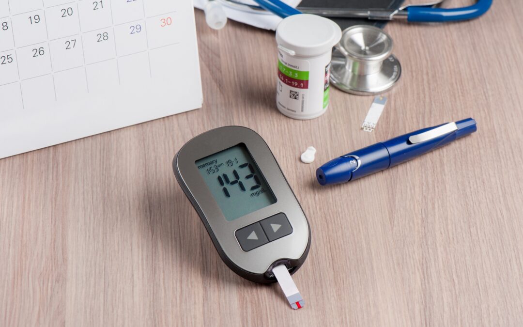 A device for checking blood sugar levels lies on a table surrounded by a calendar, pills, and a pen.
