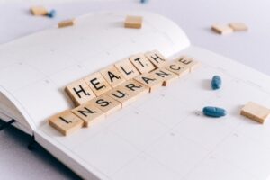 Wooden blocks spell out health insurance on a calendar with a couple of pills on top.