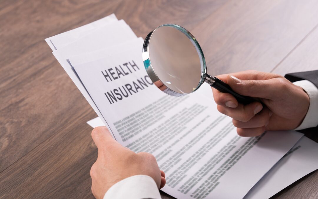 A man examines health insurance documents with a magnifying glass at the table.