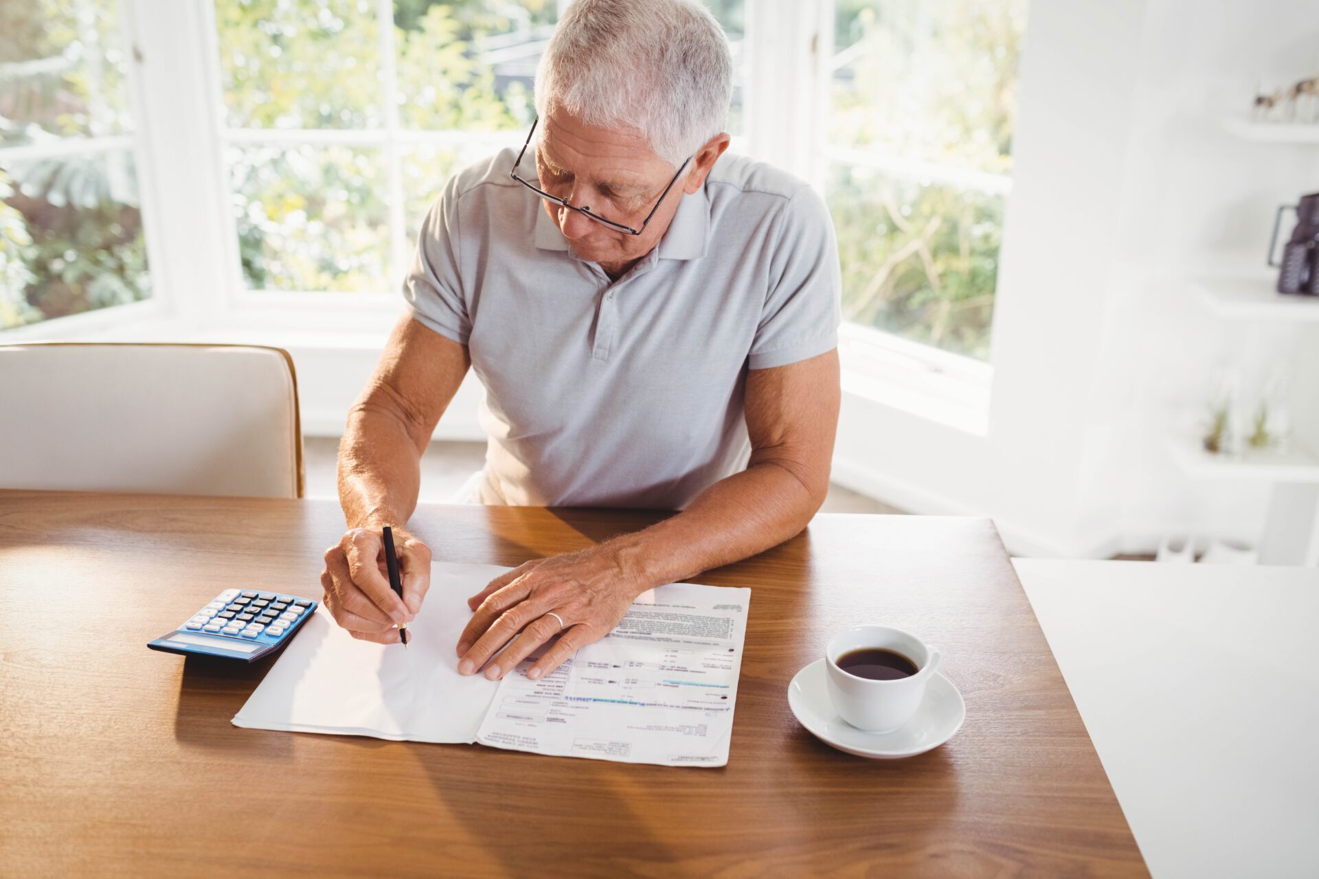 An older man signs insurance documents while sitting at a table.